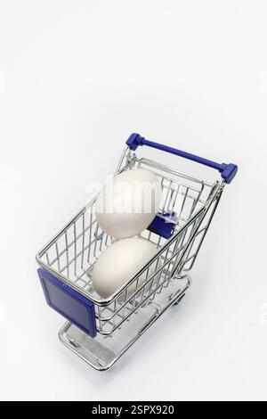Vertical shot of two white eggs in a tiny shopping cart on white with copy space. Stock Photo