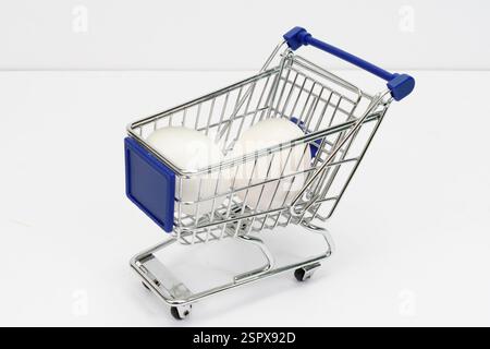 Horizontal shot of a tiny shopping cart holding two white eggs on white. Stock Photo