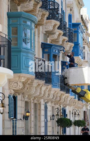 Colorful traditional balconies of Maltese in the ancient city of Valletta, Malta. Man painting Maltese windows at residential architecture Stock Photo
