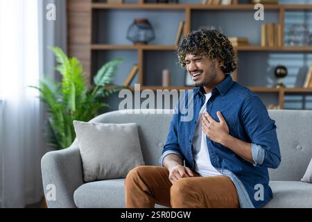 Heart attack, sick man sitting on sofa in living room at home, suffering from chest pain. Stock Photo