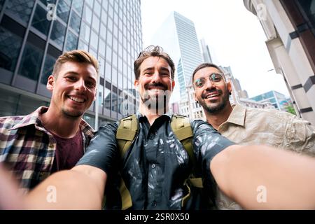 Three happy male tourists taking selfie in urban city center Stock Photo