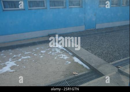 Concrete slab dividing two surfaces. One surface covered in white foam, other covered in small, smooth, grey pebbles. A blue building with many window Stock Photo