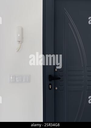 Sleek metal door with decorative patterns beside a wall-mounted intercom and light switches. Stock Photo