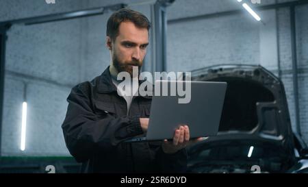 Adult man Caucasian male auto mechanic repairman using laptop checking car engine computer diagnostic transport maintenance in garage vehicle service Stock Photo