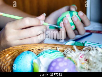 Colorful Easter eggs in foreground. Hands decorating eggs for Easter holidays. Stock Photo