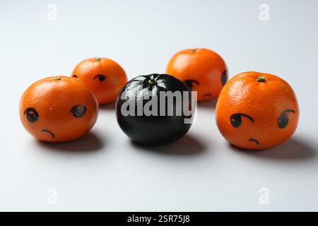 Stop racism. One black tangerine among orange ones on light background, closeup Stock Photo