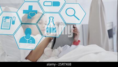 Image of medical icons over biracial girl using tablet on hospital bed Stock Photo