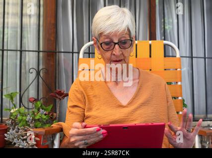 senior woman using tablet sitting in the garden by her house Stock Photo