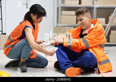 Accident at work. Woman putting bandage on her colleague's injured wrist in warehouse Stock Photo