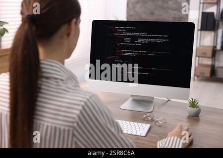 Programmer working on computer at wooden desk indoors, back view Stock Photo