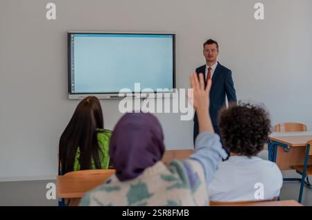 In the classroom group of college students listening to a university lecturer and engages in discussion and debate. Student raising a hand with a Stock Photo
