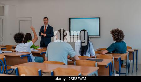 In the classroom group of college students listening to a university lecturer and engages in discussion and debate. Student raising a hand with a Stock Photo