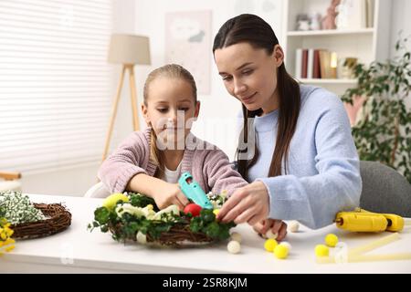 Mother and daughter with hot glue guns creating Easter composition at table indoors Stock Photo