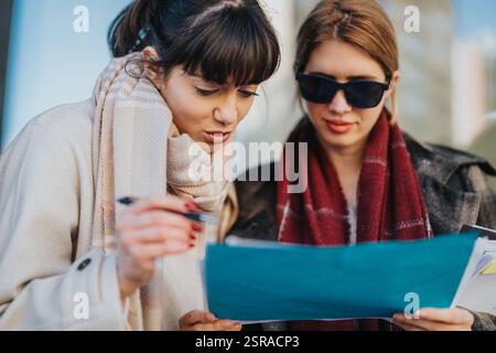 Two women collaborating on a project while reviewing documents outdoors Stock Photo