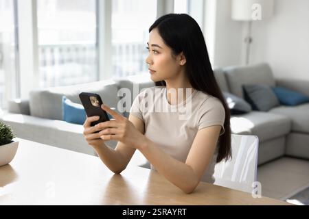 Serious Chinese young woman using smartphone at home Stock Photo
