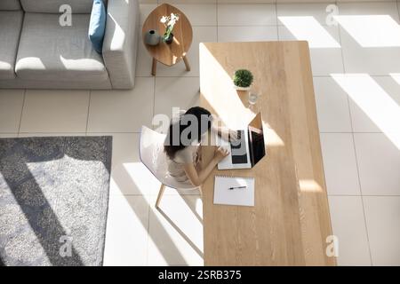 Woman working on laptop seated at table, overhead view Stock Photo
