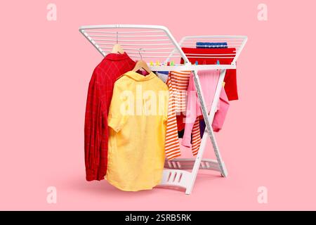 Drying rack with fresh clean laundry on light pink background Stock Photo