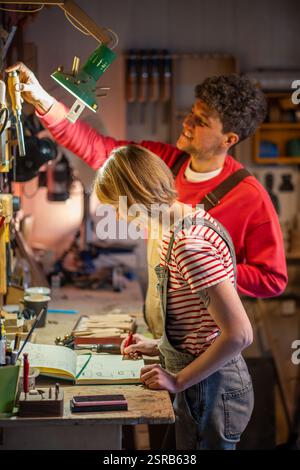 Smiling woodworker collaborate with assistant in carpentry workshop. Woman sketches furniture design Stock Photo