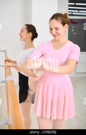 Two young female ballerinas with brown hair practice at ballet barre. They perform in bright dance studio, wearing pastel leotards, exuding focus and Stock Photo