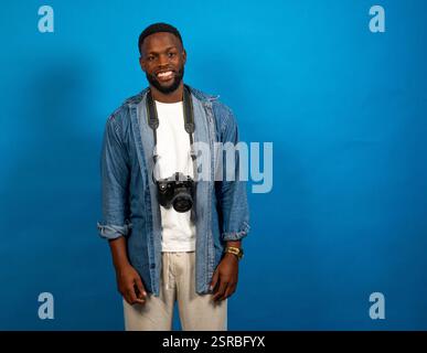 Young photographer smiling with camera hanging from neck on blue background Stock Photo
