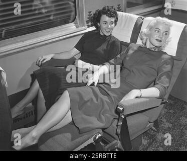 Two well-dressed young women in business attire reclining back in their seats on a train as they commute to work Stock Photo