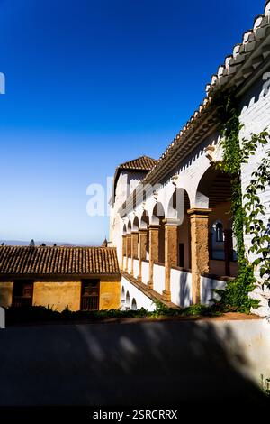 Sunlit Arches of Alhambra’s Generalife Courtyard with Terracotta Roofs and Ivy Against a Brilliant Blue Sky Stock Photo