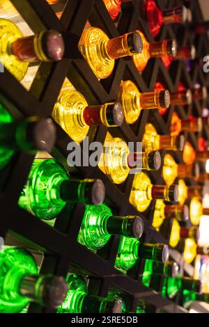 Many bottles of various colors (yellow, red, green) are displayed in a dark, geometric wine rack.  A selection of drinks. Stock Photo