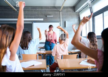 Happy group diverse elementary school students sitting in classroom attending by raising their hands Stock Photo