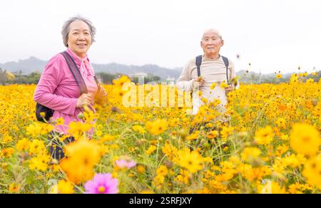 Happy senior couple hiking on trail by flowers plants at spring Stock Photo