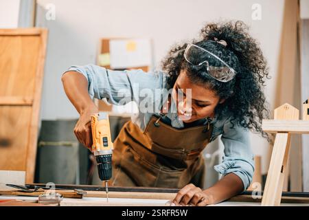 Carpenter woman using a power drill to secure a piece of wood in a workshop, focusing on precision Stock Photo