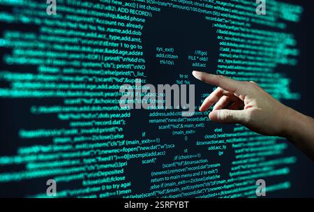 Human hand points at abstract Modern tech of Programming code screen with skull. Computer Virus, Malware, and Hacker Attack Concept. Stock Photo
