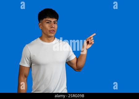 Young man wearing white t-shirt pointing his finger to the right on blue background Stock Photo