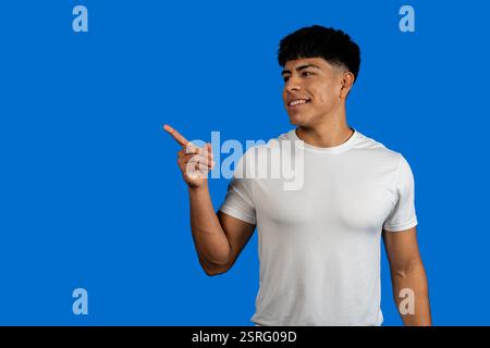 Smiling young man pointing his finger to the side showing something on a blue background Stock Photo