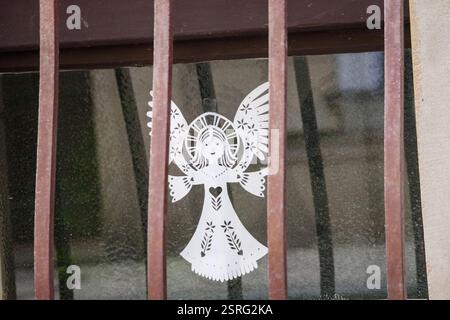 a window with metal bars behind which a decorative paper angel can be seen. Stock Photo