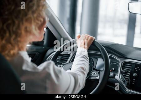 Rear view. Woman with curly blonde hair is in autosalon. Stock Photo