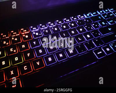 Backlit laptop keyboard with RGB lights that change color in different sections. The illumination varies between red, blue and violet tones, creating Stock Photo