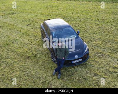 Man leaning against a black car on a green field, e-car sharing, Deer Mobility, MG4, Calw, Germany, Europe Stock Photo