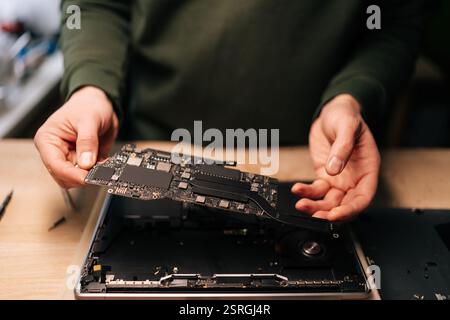 Closeup of unrecognizable technician carefully holding motherboard repairing laptop in workshop, demonstrating expertise in computer hardware Stock Photo