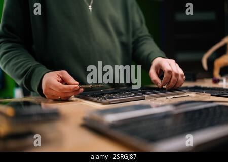 Skilled computer master carefully repairing laptop motherboard, using precision screwdriver while performing detailed electronic maintenance. Stock Photo