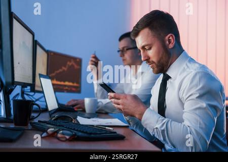 Holding smartphone in hands. Two stock traders working in the office with exchange technology. Stock Photo