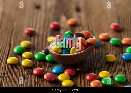 Easter concept, colorful candies in chocolate egg, close-up, macro, wooden background, rustic style Stock Photo