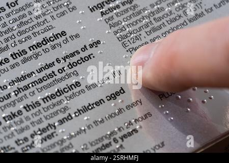 A man's finger touching braille on a box of sore throat lozenges, UK. Braille is a tactile writing system for blind and partially sighted people Stock Photo