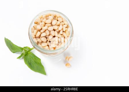 A jar of pine nuts with fresh basil leaves on white background, great forhomemade pesto, salads, and Mediterranean dishes Stock Photo