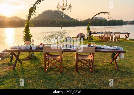 Rustic and romantic elegant outdoor dining setup with wooden long table, chairs, tableware, cutlery, candle and flora decoration in the sunset Stock Photo