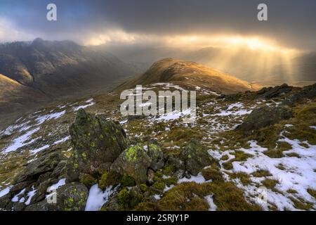 Golden sunrise over Lake District mountains with dark dramatic clouds over The Langdale Valley. Stock Photo
