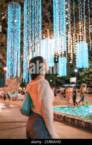 Cheerful young asian woman admire vibrant colorful light up display in urban festive celebration Stock Photo