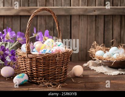 Easter eggs in a basket and bowl with purple daisies on rustic wooden background Stock Photo