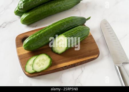 Cut in half cucumber on a wooden cutting board. Cooking vegetarian salad of green long cucumbers. Organic vegetables, healthy eating, harvest concept. Stock Photo