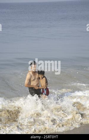 South Asian Indian father and son playing in surf waves on seashore, Shiroda, Dist. Sindhudurga, Maharashtra, India MR#703D, 703G Stock Photo
