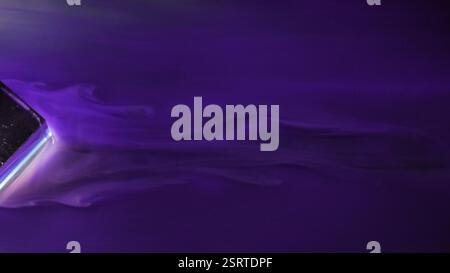 Wavy purple. Paint overflow. Smooth leak of violet liquid with misty blur curls abstract background. Colored ink swirl on glossy water surface bypassing glass cube. Stock Photo